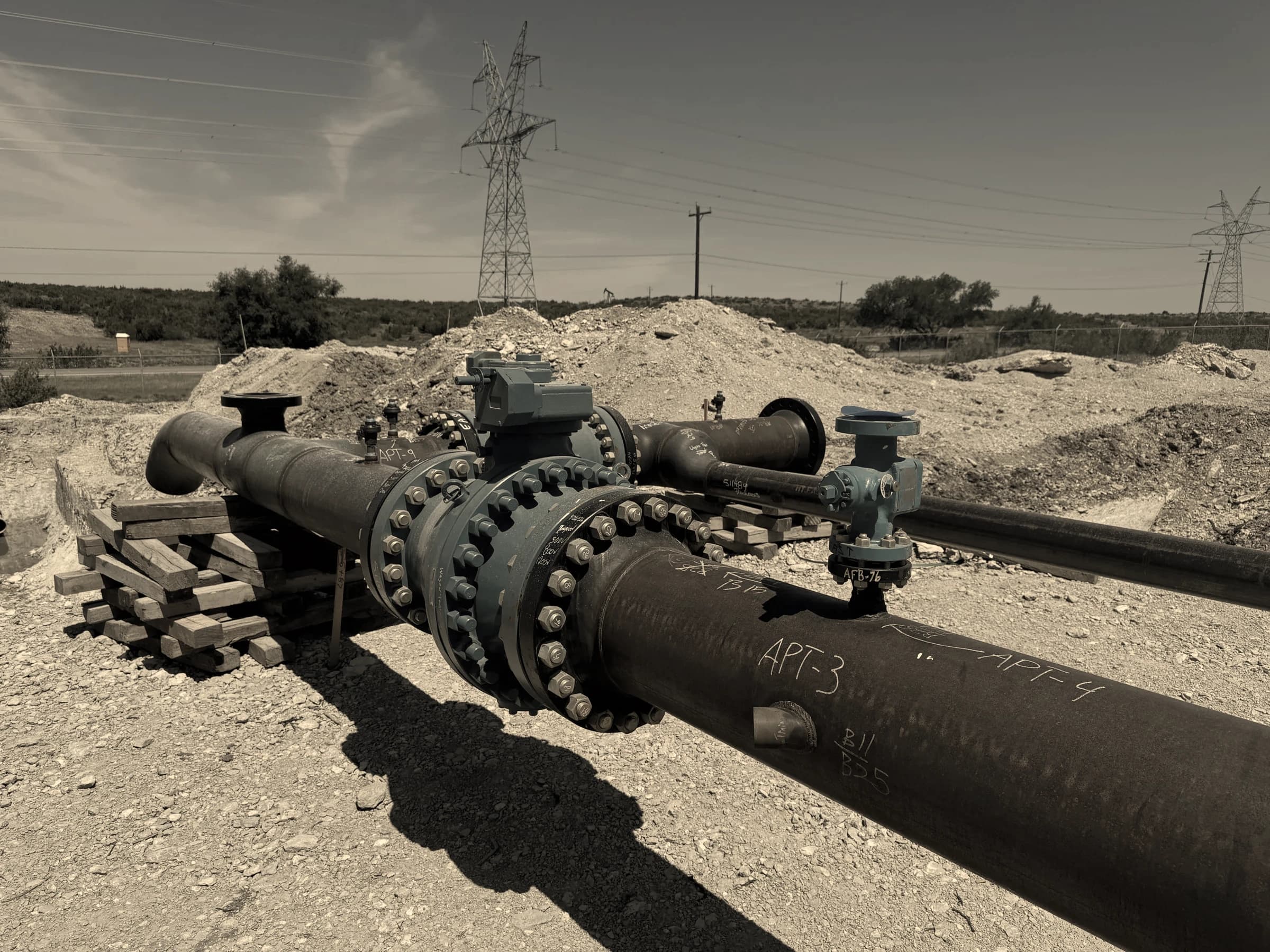 Flanged pipeline valve assembly with blue-painted fittings on a coated steel line at a graded worksite under a clear sky