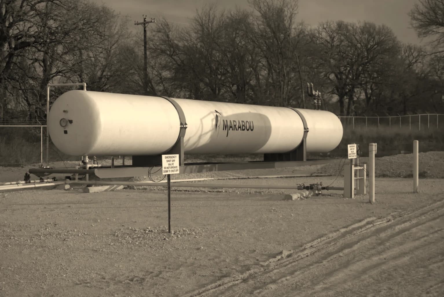 A horizontal bullet storage vessel on steel saddles at a fenced site, with connecting pipework and bollards on a graded pad